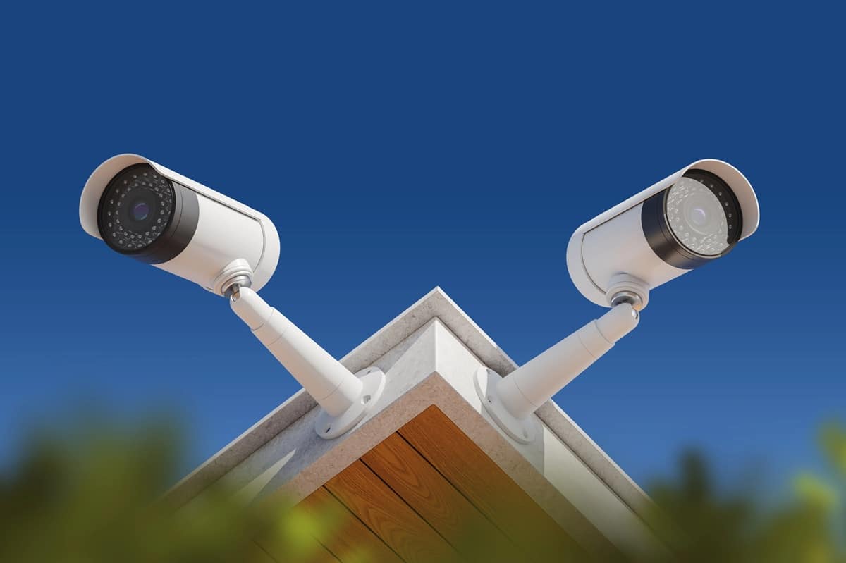 Two surveillance cameras mounted on the corner of a building under a clear blue sky.