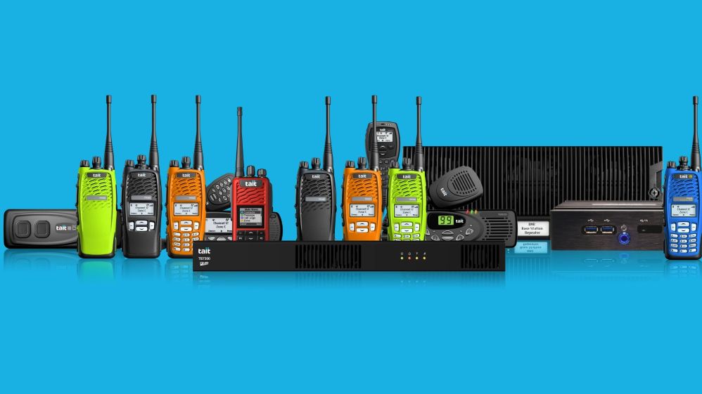 A line-up of Tait DMR radios and communication equipment in various colours, displayed against a blue background, used for professional radio communications.